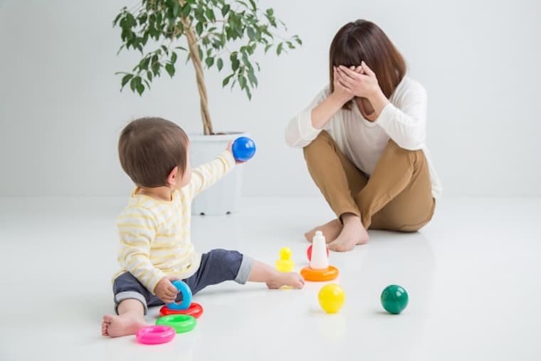 おもちゃを散らかす赤ちゃんと泣く女性
